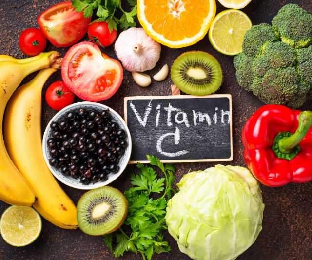 The text vitamin C written on wooden surface with different fruits and vegetables around it