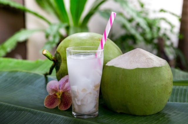 a glass of coconut water standing next to two green coconuts