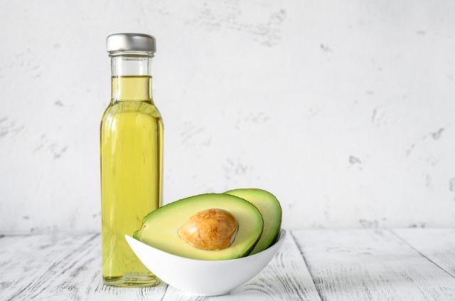 A bottle of olive oil standing next to a bowl of avocado