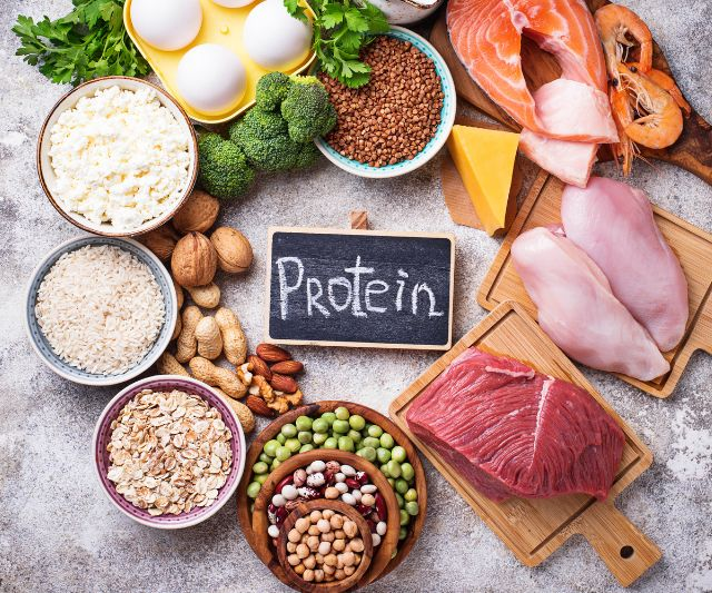 a text saying protein written on a small black board with protein rich foods around it