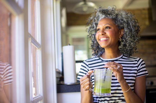 a cheerful woman holding a green smoothie glass in her hand