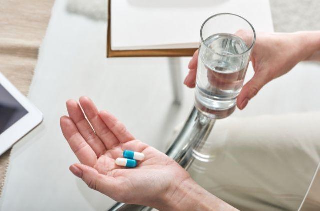 a person holding pills in one hand and a glass of water in another