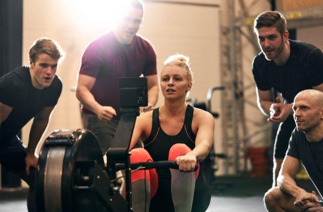 a woman on a rowing machine surrounded by fitness trainers (Are Rowing Machines Good for Weight Loss?)