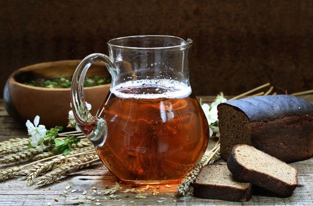 a glass pitcher filled with kvass next to sliced bread
