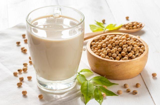 a glass of milk next to a bowl of soy seeds
