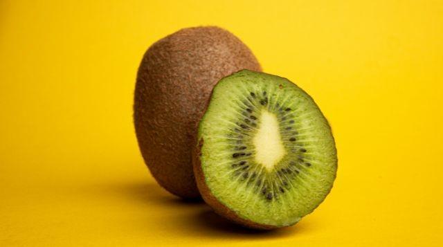 A whole kiwi with a sliced half in front, showcasing the bright green interior, on a yellow background. (Is Kiwi Good For Weight Loss?)