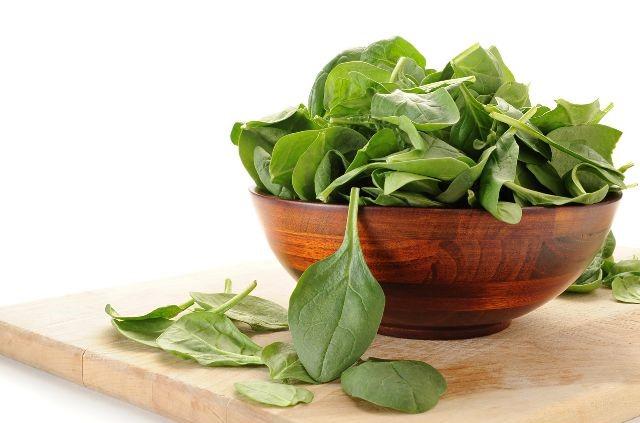 A wooden bowl filled with fresh spinach leaves on a cutting board, showcasing the raw vegetable ready for use. (Is Spinach Good For Weight Loss?)