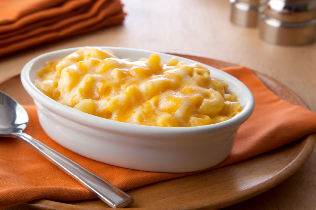 A bowl of creamy macaroni and cheese on a wooden tray with an orange napkin and silver spoon on the side. (Is Mac and Cheese Good For Weight Loss?)