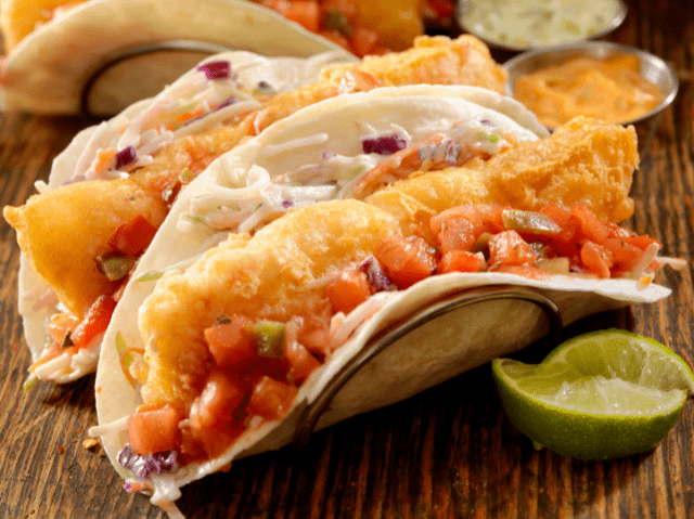 Fish tacos with crispy battered fish, fresh toppings, and a lime wedge in soft tortillas.