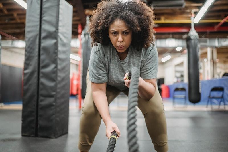 A focused woman doing a high-intensity battle rope workout in a gym, showing determination and strength.