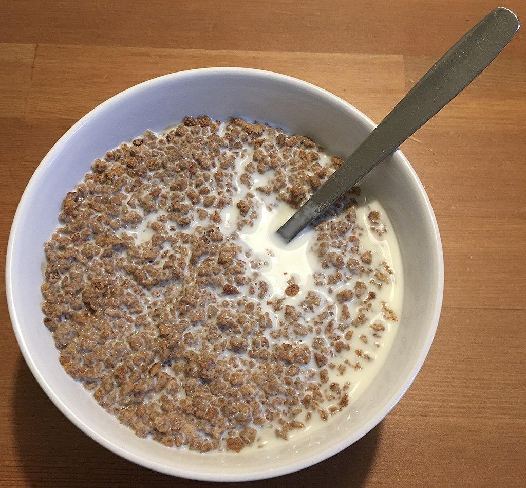 A bowl of whole grain cereal with milk and a spoon on a wooden table.  (are grape nuts good for weight loss)