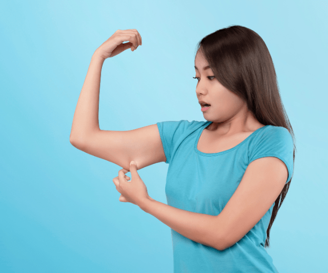 A young woman measuring her upper arm muscles with a tape measure, looking concerned about muscle loss.