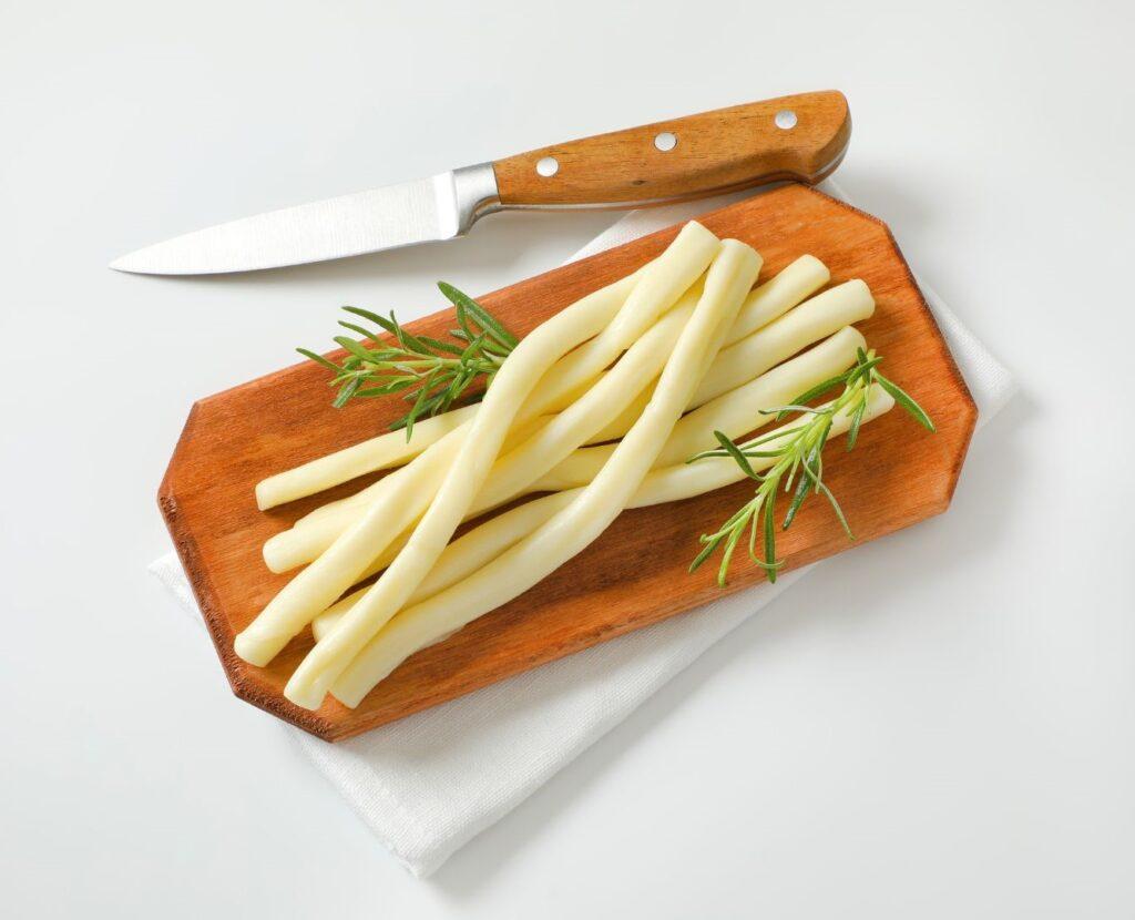 A wooden cutting board with string cheese and a sprig of rosemary next to a kitchen knife. ( Is String Cheese Good for Weight Loss? )