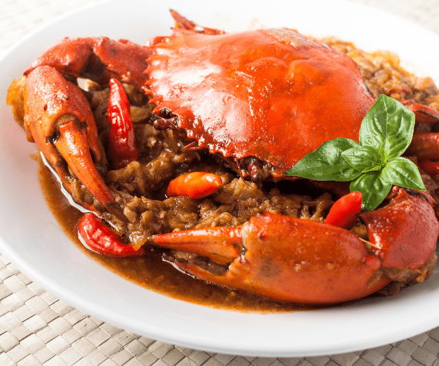 A cooked crab served with a savory sauce on a white plate, garnished with basil and chilies. (Is Crab Good For Weight Loss?)
