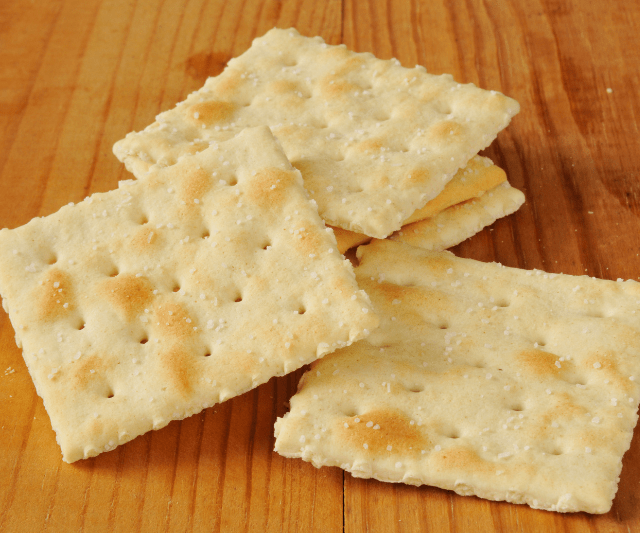 A stack of Saltine crackers on a wooden surface. (Are Saltine Crackers Good For Weight Loss?)