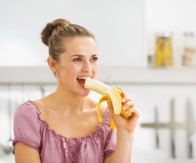 A cheerful woman playfully eating a banana.