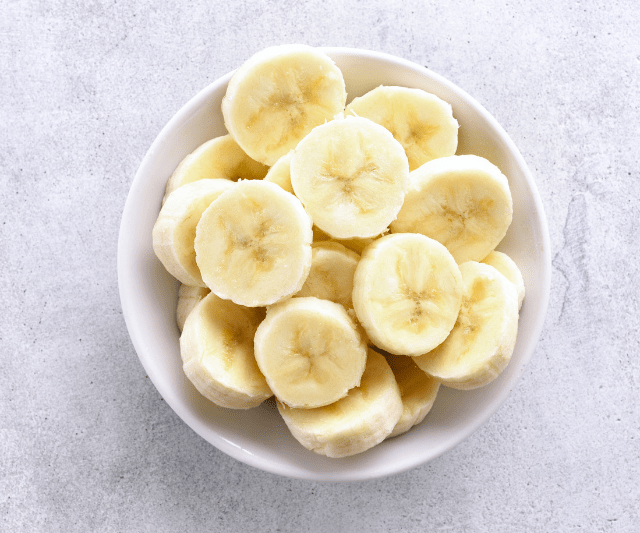 Bowl of sliced bananas on a light grey background.