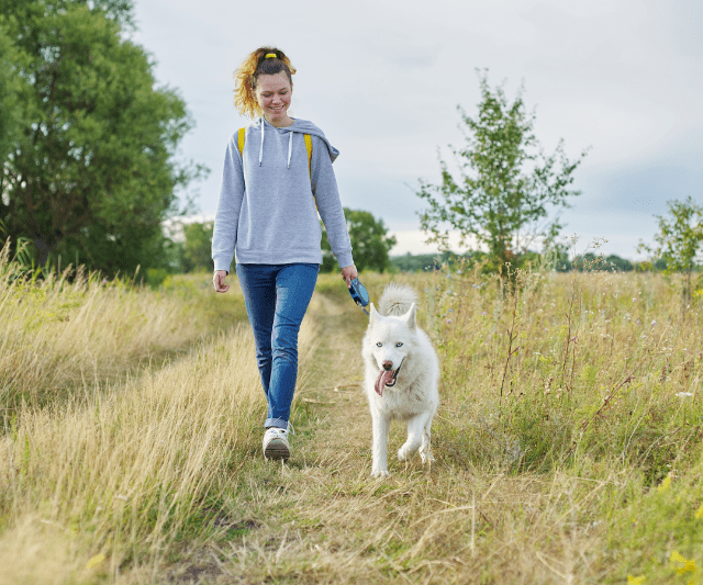 Woman walking a white dog on a grassy path outdoors.