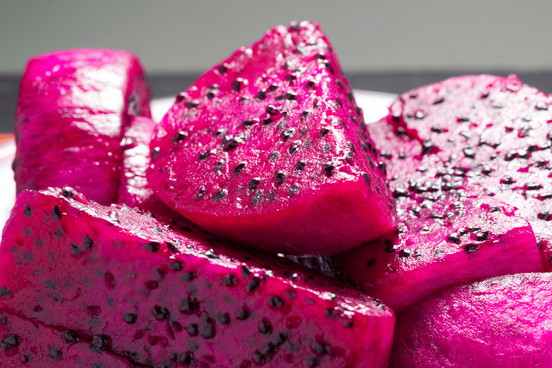 Close-up of vibrant pink dragon fruit slices with black seeds, showcasing the fruit's juicy texture and bright color.